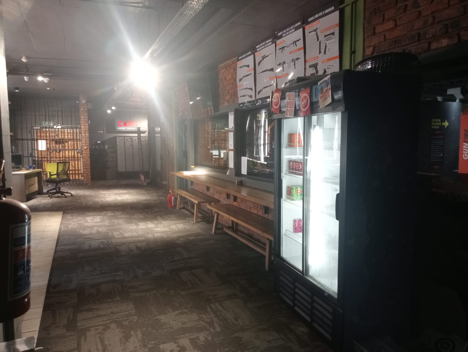 Shop floor with firearm safety posters, drinks fridge and the safe room gate