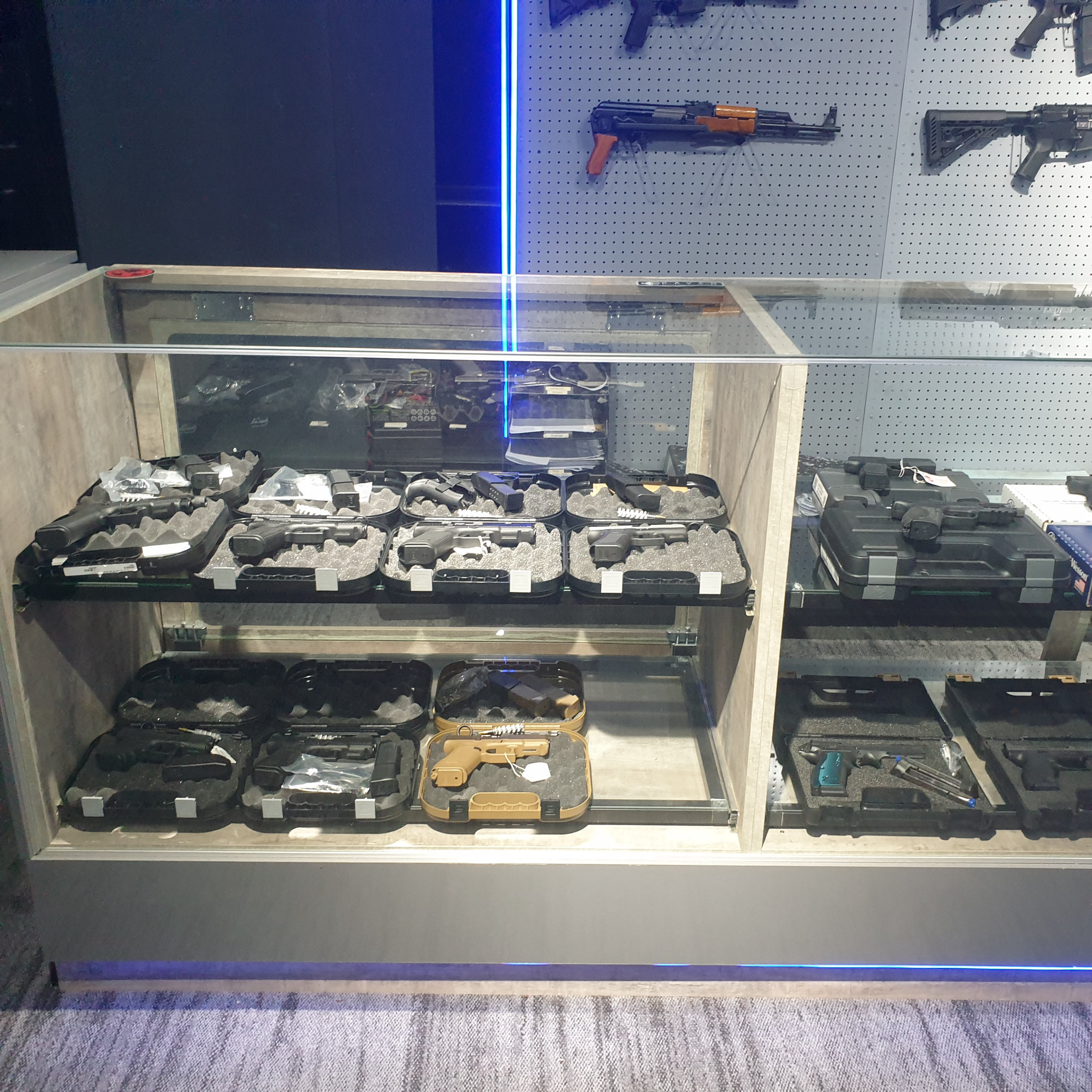 Glass counter with pistols in foam-cut cases below the AK-pattern shotgun display