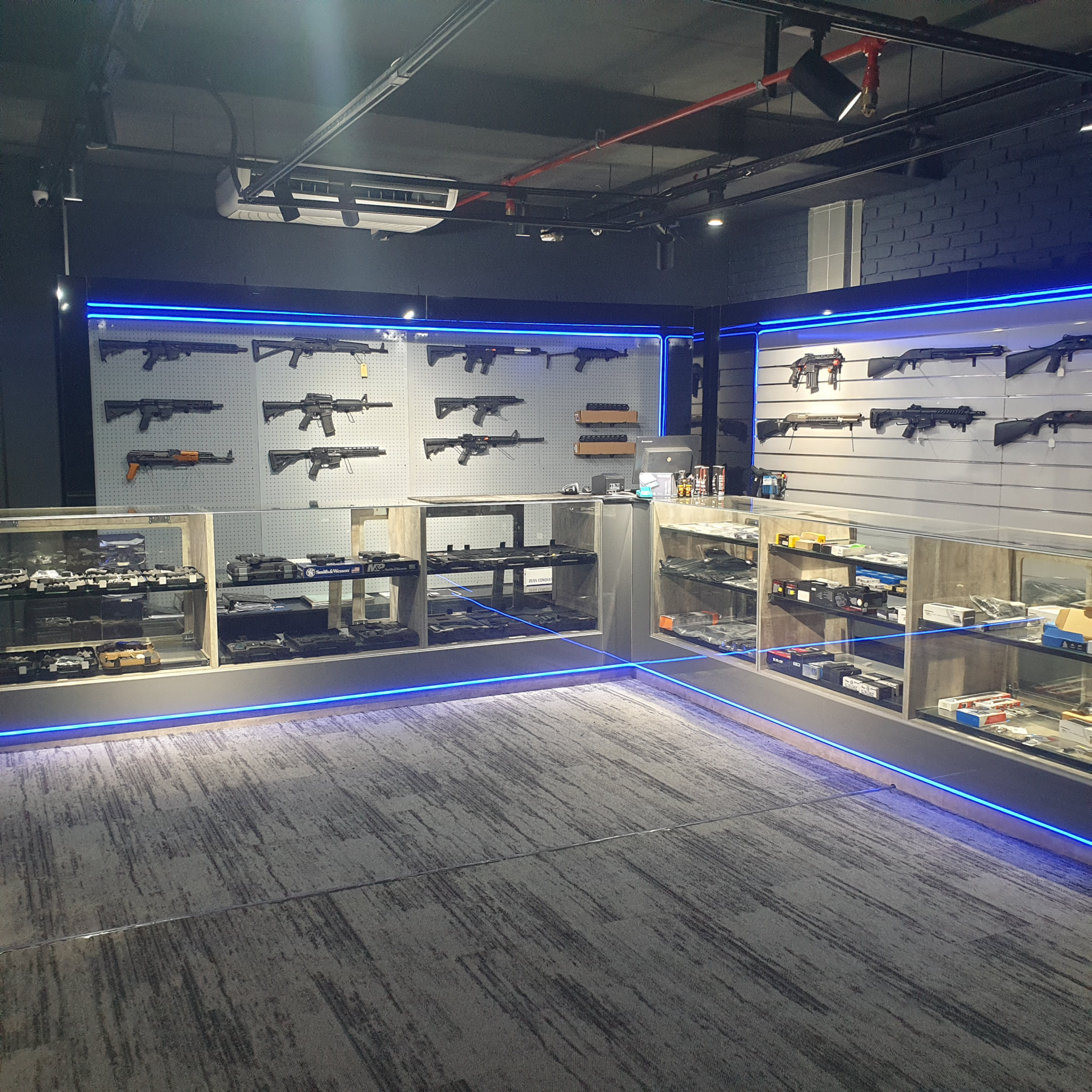 Wide corner view of the sales floor: rifle pegboard, shotgun slatwall and the glass display counters